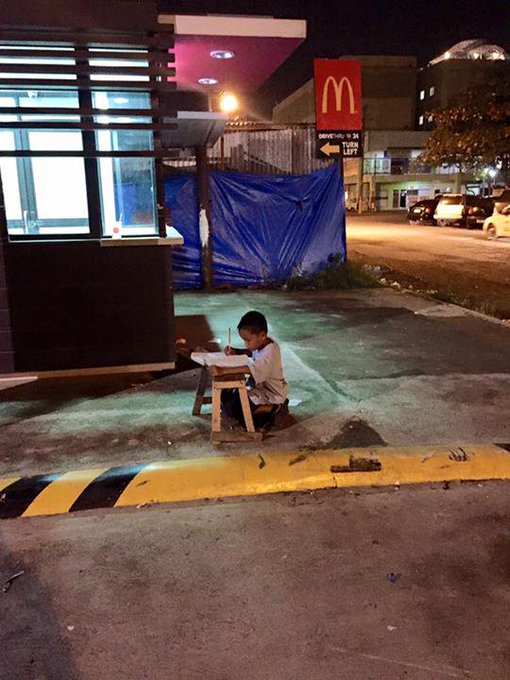 Le garçon de 9 ans fait ses devoirs dans la rue sous la lumière d’une enseigne